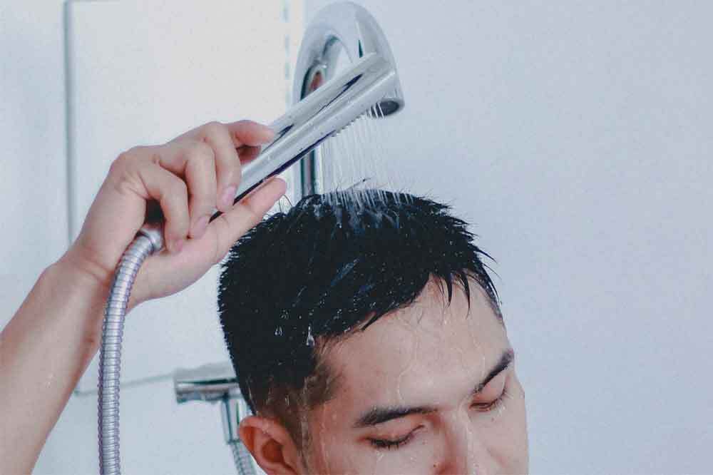 シャワーで頭を濡らす男性